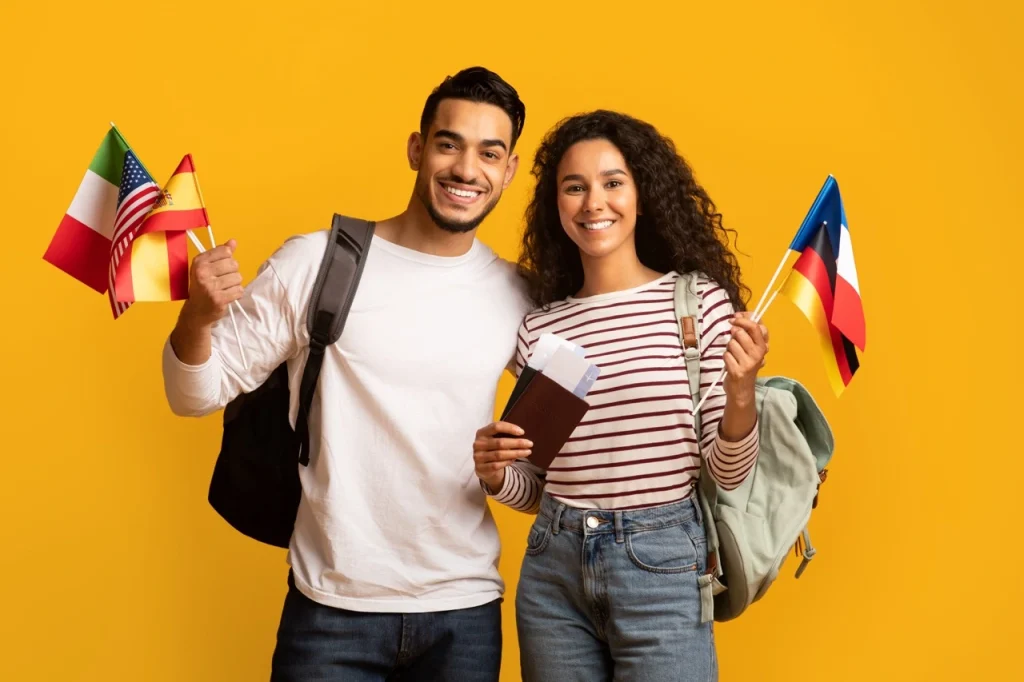 Two Students Smiling, Holding International Flags And Passports, Ready For Their Study Abroad Journey With Student Visas.